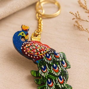 May include: A hand-painted peacock keychain. The wooden charm features a blue head, a red and multicolored body, and a green tail with white, blue, and red accents. The keychain has a gold-colored chain and ring.