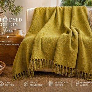 Könnte beinhalten: Ein senfgelber Baumwoll-Wurf mit gewebter Textur und Fransen, drapiert über einem cremefarbenen Sofa. Das Bild enthält den Text "SOLID DYED COTTON Throw" und "SIMPLE. SOFT. BEAUTIFULLY HANDWOVEN." Der Wurf ist weich, atmungsaktiv und leicht.