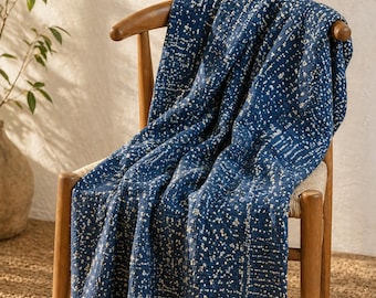 Acogedora manta tradicional estampada a mano sobre una silla de madera en un espacio minimalista luminoso y soleado, con texturas naturales que crean un ambiente cálido.