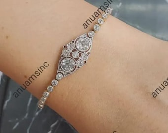 May include: A silver and gold bracelet with a central ornate design featuring two large, round, clear gemstones. Smaller, round gemstones are set along the bracelet's length. The bracelet is on a wrist.