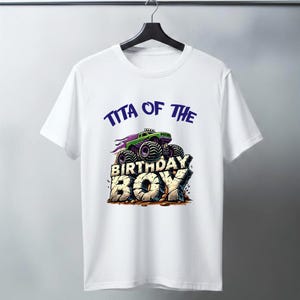 May include: White t-shirt featuring a green and purple monster truck design with the text "TITA OF THE BIRTHDAY BOY" in blue and beige. The graphic is centered on the front of the shirt.