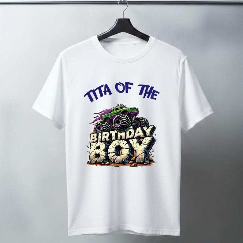 May include: White t-shirt featuring a green and purple monster truck design with the text "TITA OF THE BIRTHDAY BOY" in blue and beige. The graphic is centered on the front of the shirt.