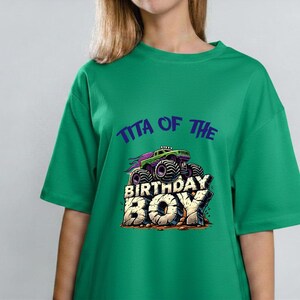 May include: Green t-shirt with the text "Tita of the Birthday Boy" and a graphic of a monster truck. The monster truck is purple, green, and black. The text is in a bold, playful font.