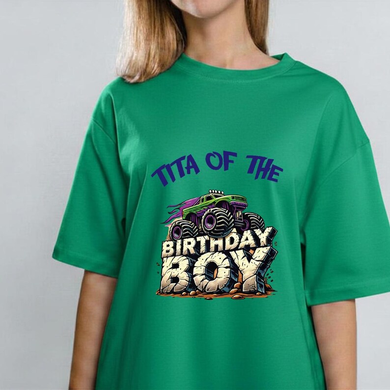 May include: Green t-shirt with the text "Tita of the Birthday Boy" and a graphic of a monster truck. The monster truck is purple, green, and black. The text is in a bold, playful font.