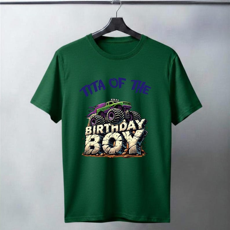 May include: A green t-shirt featuring a graphic of a monster truck with the text "TITA OF THE BIRTHDAY BOY" in purple and white. The monster truck is purple and green with large black tires. The text "BIRTHDAY BOY" is in a stone-like font.