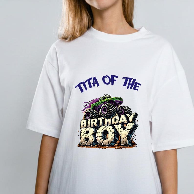 May include: White t-shirt featuring a graphic of a green monster truck with purple flames and the text "TITA OF THE BIRTHDAY BOY" in blue and gold. The design is centered on the front of the shirt.