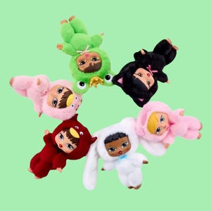 May include: A collection of plush dolls in various animal costumes, including a frog, cat, bunny, and bird. The dolls have large eyes and are in shades of green, black, white, red, and pink. The background is a light green.