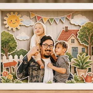 Könnte beinhalten: Ein 3D-Schattenbox-Rahmen mit einer mehrschichtigen Papierbastelszene und einem zentralen Foto eines Erwachsenen mit zwei Kindern. Der Hintergrund zeigt ein Haus, Bäume, eine Sonne, Wolken und Wimpel in einem weißen rechteckigen Rahmen.
