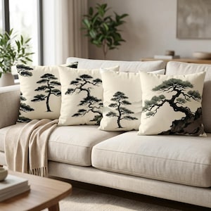 Könnte beinhalten: Vier quadratische Kissen mit cremefarbenem Hintergrund und japanischen Baumdesigns in Schwarz und Grün. Die Kissen sind auf einem beigen Sofa mit einer beigen Decke angeordnet.