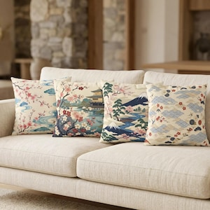 Könnte beinhalten: Vier dekorative Kissen mit japanisch inspirierten Designs auf einem beigen Sofa. Die Kissen zeigen Kirschblüten, Berge, Tempel und Wellenmuster in Rosa-, Blau- und Beigetönen.
