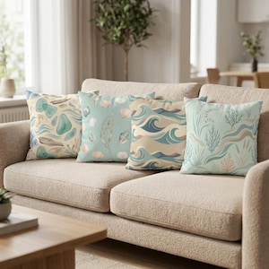 Op de afbeelding: Vier decoratieve sierkussens met kustontwerpen liggen op een beige bank. De kussens hebben patronen van golven, schelpen en abstracte vormen in tinten blauw, beige en blauwgroen. De kussens voegen een vleugje charme toe aan de woonkamer.