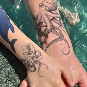 Puede incluir: Dos brazos y una mano con tatuajes de pulpo a juego en tinta negra. Los tatuajes son detallados, con los tentáculos del pulpo envolviendo el brazo y la mano. El fondo es una piscina turquesa.