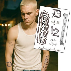 Puede incluir: Una persona con una camiseta sin mangas blanca y vaqueros azules. La persona tiene tatuajes en los brazos que dicen "Slim Shady", "Proof" y "D". Una hoja de tatuajes temporales está en el fondo.
