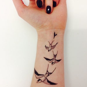 May include: A close-up of a person's wrist with a tattoo of three black birds flying in formation.