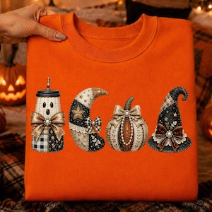 May include: An orange sweatshirt featuring a graphic print of four items: a ghost-shaped jar with a bow, a crescent moon with a star, a pumpkin with a bow, and a witch hat with a bow. The designs incorporate black, white, and tan patterns.