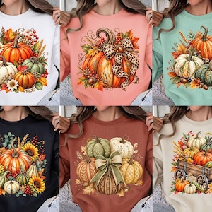 May include: A collection of six crewneck sweatshirts in various colors, each featuring a printed graphic of pumpkins, autumn leaves, berries, and wheat. The designs include pumpkins in orange, white, and green, with some featuring bows or a wooden wagon.