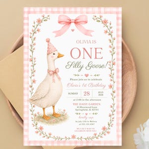 May include: A birthday invitation card featuring a white goose wearing a pink polka dot party hat and bow. The card has a pink gingham border, floral wreath, and text reading: Olivia is one silly goose, Olivia's 1st birthday, July 28, 2026.