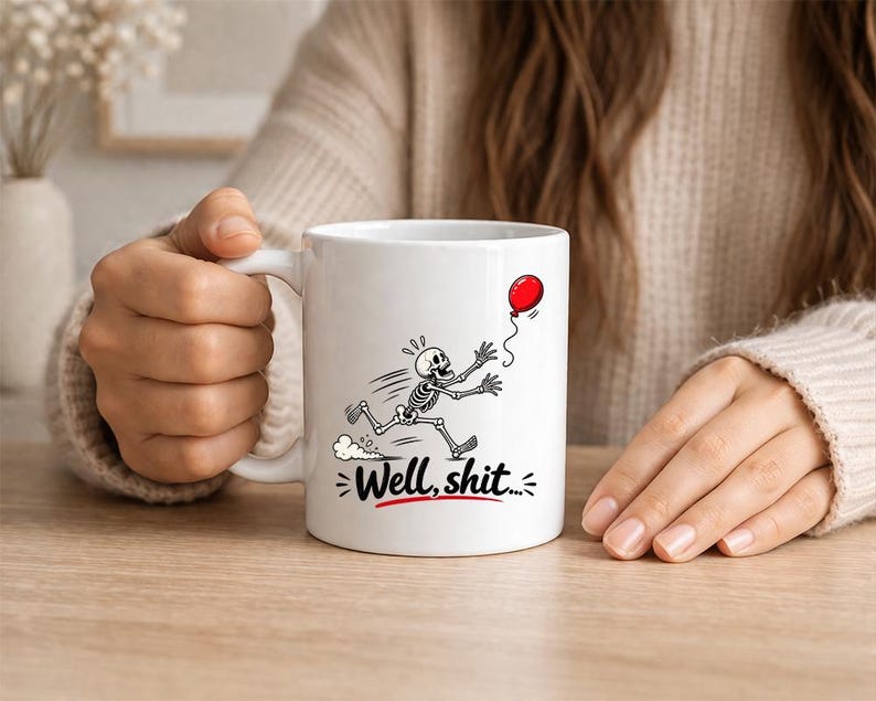 May include: A white ceramic mug featuring a black and white illustration of a skeleton running after a red balloon. Below the skeleton, the text "Well, shit..." is printed in black letters with a red underline, centered on the mug's exterior.