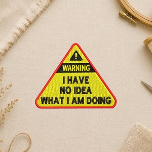 May include: Embroidered patch in a yellow triangle shape with a red border. The patch features the text "WARNING I HAVE NO IDEA WHAT I AM DOING" in black letters.