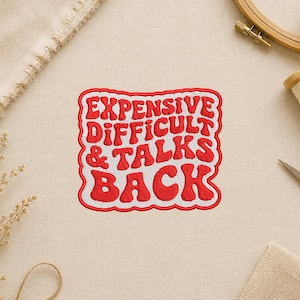 May include: Embroidered patch with the text "EXPENSIVE DIFFICULT & TALKS BACK" in red, outlined in white and red. The patch is rectangular with rounded corners. The background is a light beige fabric.