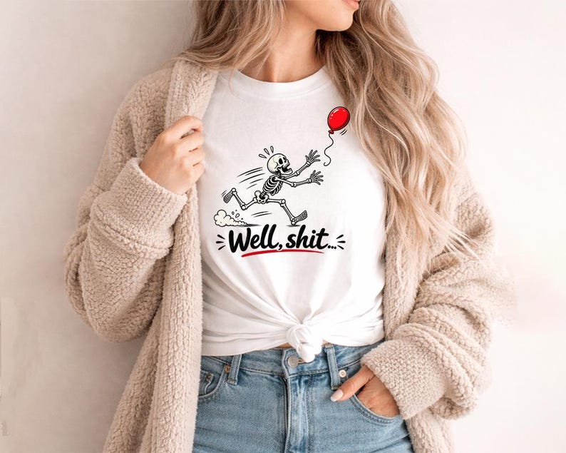 May include: A white t-shirt featuring a black and white graphic of a skeleton running after a red balloon. Below the skeleton, the text "Well, shit..." is printed in a bold black script font with a red underline accenting the phrase.