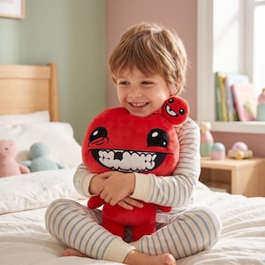 Peut inclure: Un enfant souriant serre un grand jouet en peluche rouge avec un large sourire et des yeux noirs. Le jouet a une version plus petite attachée. L'enfant porte un pyjama rayé et est assis sur un lit.