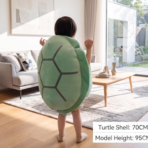 May include: A light green turtle shell costume with a dark gray geometric pattern. The shell measures 70cm. The model's height is 95cm. The costume is designed for children and is made of soft material.