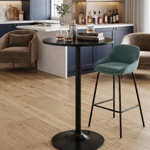 May include: A black round bar table with a black base and a teal upholstered bar stool. Two brown armchairs are in the background. Two glasses, a cocktail shaker, and books are on the table. The table is 30 inches in diameter.