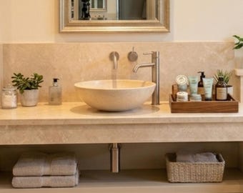 Peut inclure: Une vasque en pierre beige est posée sur un comptoir en pierre assorti avec un robinet en métal brossé. Un plateau en bois contient divers articles de toilette, tandis qu'un panier tressé et des serviettes pliées sont sur l'étagère inférieure.