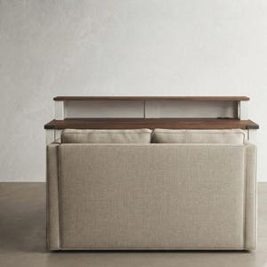 May include: A beige upholstered sofa positioned in front of a wooden console table. The sofa features two rectangular back cushions with a textured fabric finish. The console table has a dark brown wooden top and a white frame with metal accents.