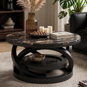 May include: A round coffee table with a black marble top featuring gold veining and a black curved base. The table includes a lower shelf holding a small bowl and eyeglasses, while the top surface displays a glass vase, candles, and books.