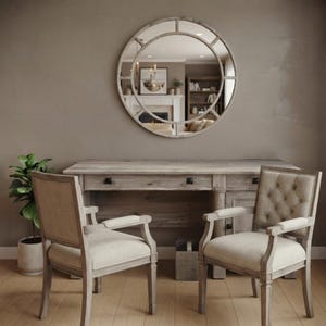 May include: A round wall mirror with a light wood frame featuring a segmented circular design, positioned above a light wood desk with three drawers and two upholstered armchairs with tufted backrests and light beige fabric seats.