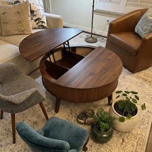 May include: A round, dark wood coffee table with a lift-top mechanism that reveals a divided storage compartment inside. The table features a slatted exterior design and stands on four tapered wooden legs, showcasing a rich, natural wood grain.