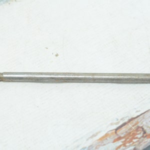 Op de afbeelding: Een metalen gereedschap met een bruin en wit marmerachtig kunststof handvat. Het gereedschap is lang en dun, met een puntig uiteinde.