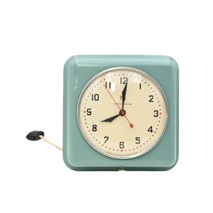 Könnte beinhalten: Eine quadratische, hellblaue Wanduhr mit cremefarbenem Zifferblatt, schwarzen Ziffern und einer silberfarbenen Lünette. Die Uhr hat schwarze Stunden- und Minutenzeiger, einen roten Sekundenzeiger und eine schwarze Zugschnur links.