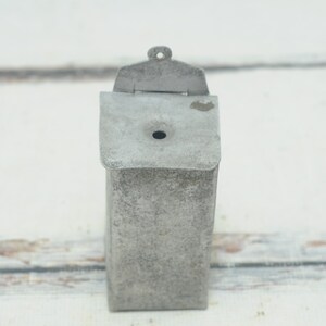 May include: A vintage metal tin with a hinged lid and a small hole in the top. The tin is weathered and has a gray finish.