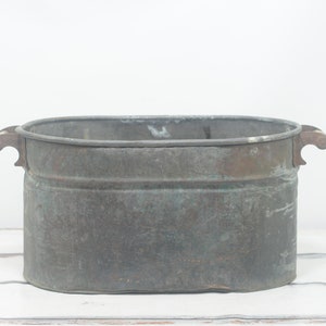 May include: A large, oval-shaped copper tub with two handles. The tub is aged and has a greenish patina.