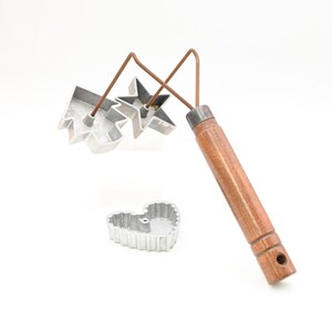 Könnte beinhalten: Ein Vintage-Ausstechersatz mit Holzgriff und drei Metallausstechern in Form eines Herzens, eines Sterns und eines Ahornblattes. Der Griff ist braun und die Ausstecher sind silberfarben.
