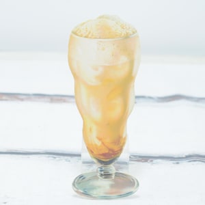May include: A tall glass filled with a creamy, light brown milkshake topped with whipped cream.