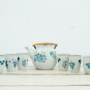 May include: A white ceramic teapot with a bamboo handle and blue floral design, accompanied by six matching teacups.
