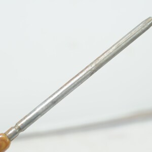 Op de afbeelding: Een close-up van de punt van een metalen schroevendraaier met een bruin en beige houten handvat.