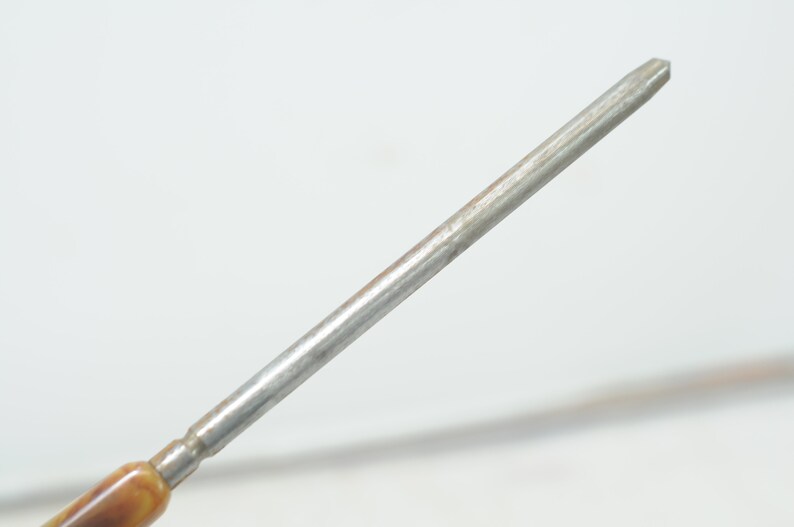 Op de afbeelding: Een close-up van de punt van een metalen schroevendraaier met een bruin en beige houten handvat.