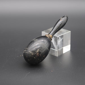 Puede incluir: Un mazo de madera negro con una cabeza redonda y un mango largo. El mazo está apoyado en un bloque de vidrio transparente.