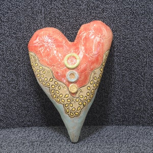 May include: A handmade ceramic heart with a red and blue glaze. The heart has a yellow and brown floral design around the edges and three round buttons in the centre.