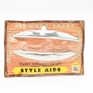 May include: Vintage package of Redwood Brand Style Aids. The package features two chrome-colored drawer pulls on a wood-grain background. The package has the text "Redwood Brand" and "Style Aids" printed on it.