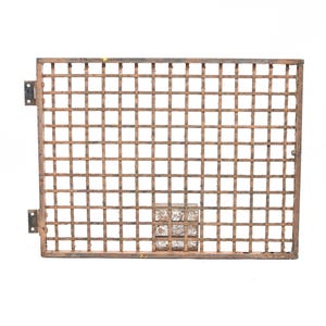 May include: A rectangular metal grate featuring a grid pattern of intersecting bars with a weathered brown finish. The structure includes two hinges attached to the left side and a small, square, textured metal plate positioned near the bottom center.