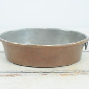 May include: A round copper baking pan with a silver interior and two small handles on the side.