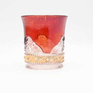 May include: A red glass tumbler with a gold rim and clear glass detailing. The glass has a textured surface and a vintage look.