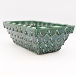 May include: Green ceramic rectangular planter with a scale-like texture. The planter has a glossy finish and a raised rim. A decorative container for plants.