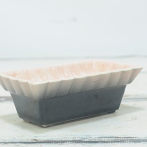 May include: A rectangular ceramic planter with a pink and grey glaze. The planter has a fluted rim and a dark grey base.